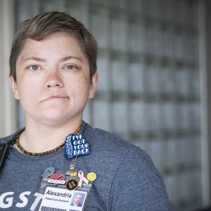Alex Paudyn has short, light brown hair and greenish/brown eyes. She’s wearing a dark blue t-shirt with a pin above our KHSC ID badge that says “I’ve got your back”. She’s pictured in a hallway at Kingston General Hospital.