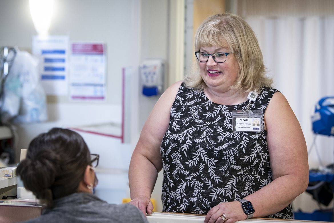 People of KHSC: Nicole Chenier-Hogan Nicole Chenier-Hogan is pictured standing next to a unit care desk. She’s looking down and speaking with a nurse sitting at the care desk.