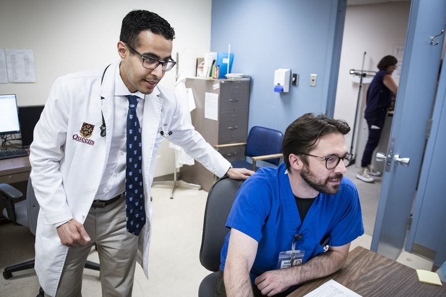 Dr. Almufleh is seen standing behind a colleague who is sitting at desk. The duo are looking over information on a computer screen.