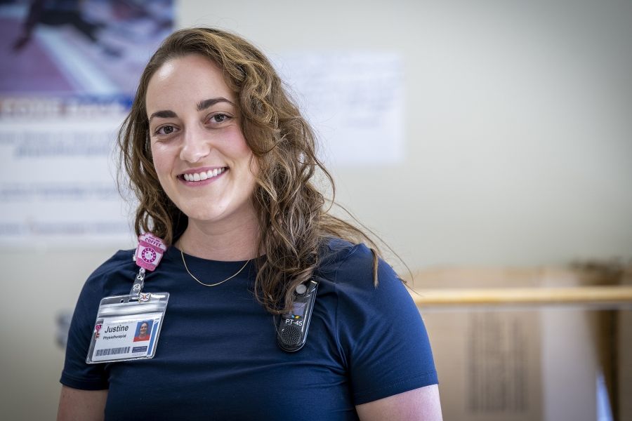 PeopleOfKHSC_Justine_White_1 Justine White is photographed smiling directly into the camera. She has shoulder length, medium brown, wavy hair and brown eyes. She’s wearing a navy blue shirt with her KHSC ID badge.