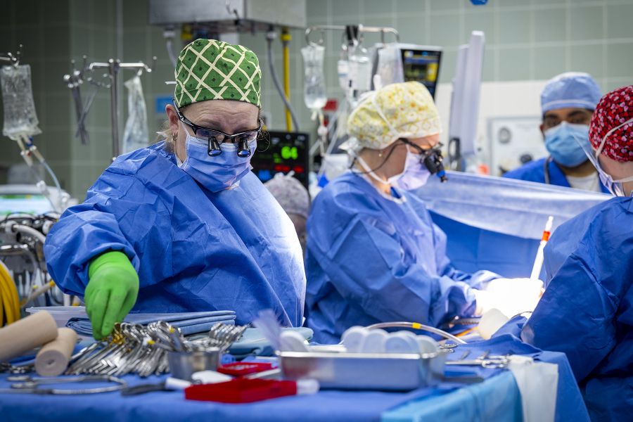 Tammy Richards is in the middle of surgery, about to grab some instruments from a table. She’s wearing blue scrubs, gown, mask, a scrub cap and specialized glasses.