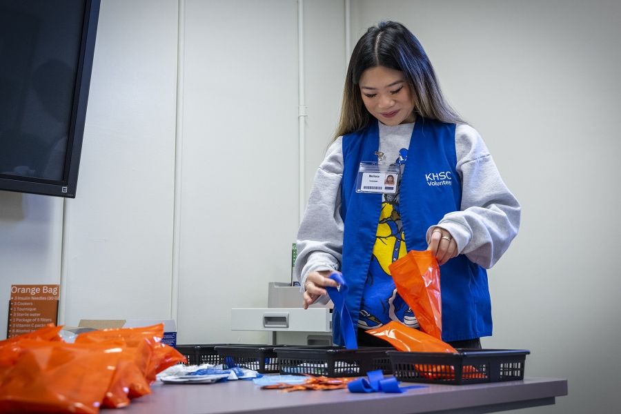 A volunteer is standing, putting together an orange grab bag filled with items.