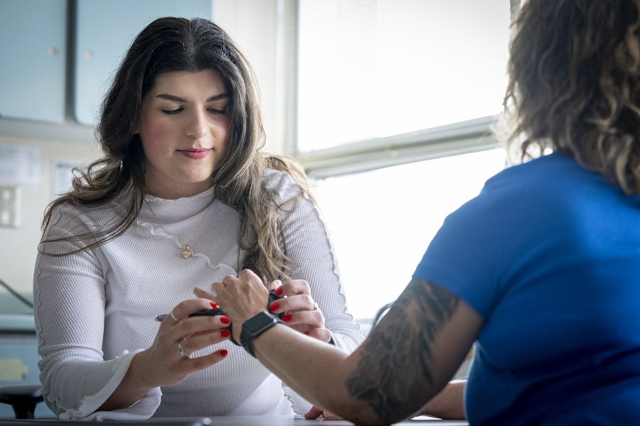 PeopleOfKHSC_Andreea_Bocicariu_7 Andreea Bocicariu is sitting at a table in the Orthopedics and Plastics Clinic, across from a patient whose back is to the camera. She’s looking down at her patient’s hand, while wrapping a splint on it.