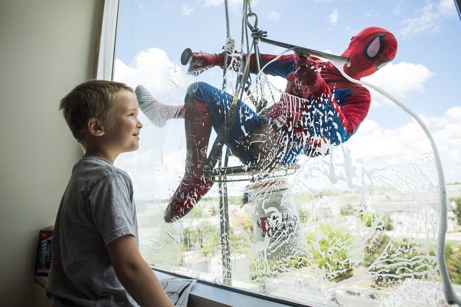 a young boy looks out a window as it is being washed by Spiderman
