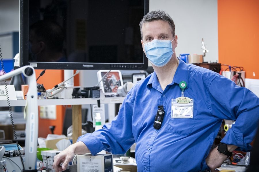 Stéphane Bois has short, salt and pepper hair. He’s wearing a long-sleeve blue shirt and mask. He’s picture inside the Clinical Engineering department at the Kingston General Hospital site.