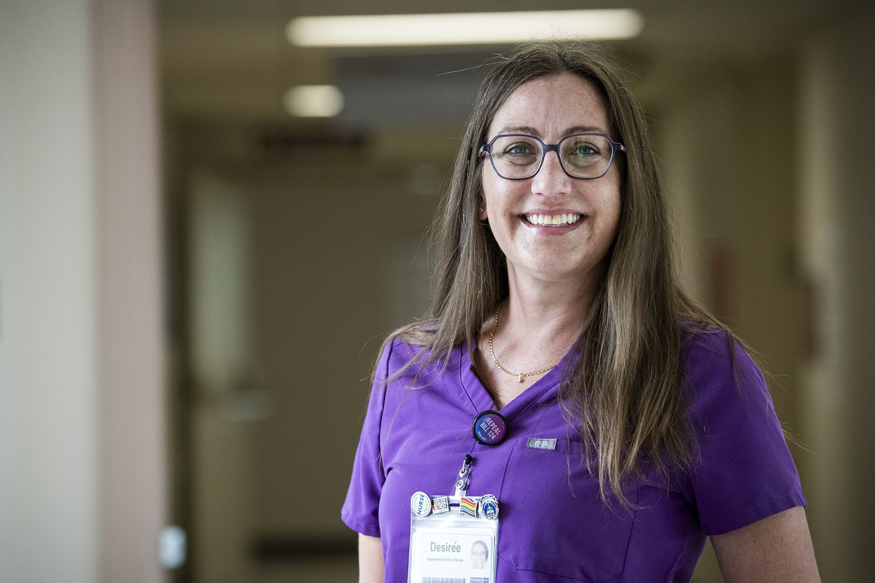 Desirée vandenTillaart is photographed standing in a hallway at the Kingston Bariatric Centre of Excellence, located at the Hotel Dieu Hospital site. She has straight, medium brown hair that goes past her shoulders. She has blue eyes, wears glasses and is wearing purple scrubs. 