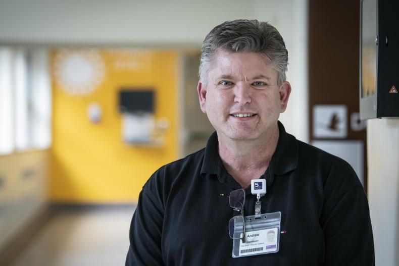 Andrew Schick is photographed standing in a hallway at the Kingston General Hospital site. He has short, salt and pepper hair, blue eyes and is wearing a black polo shirt.