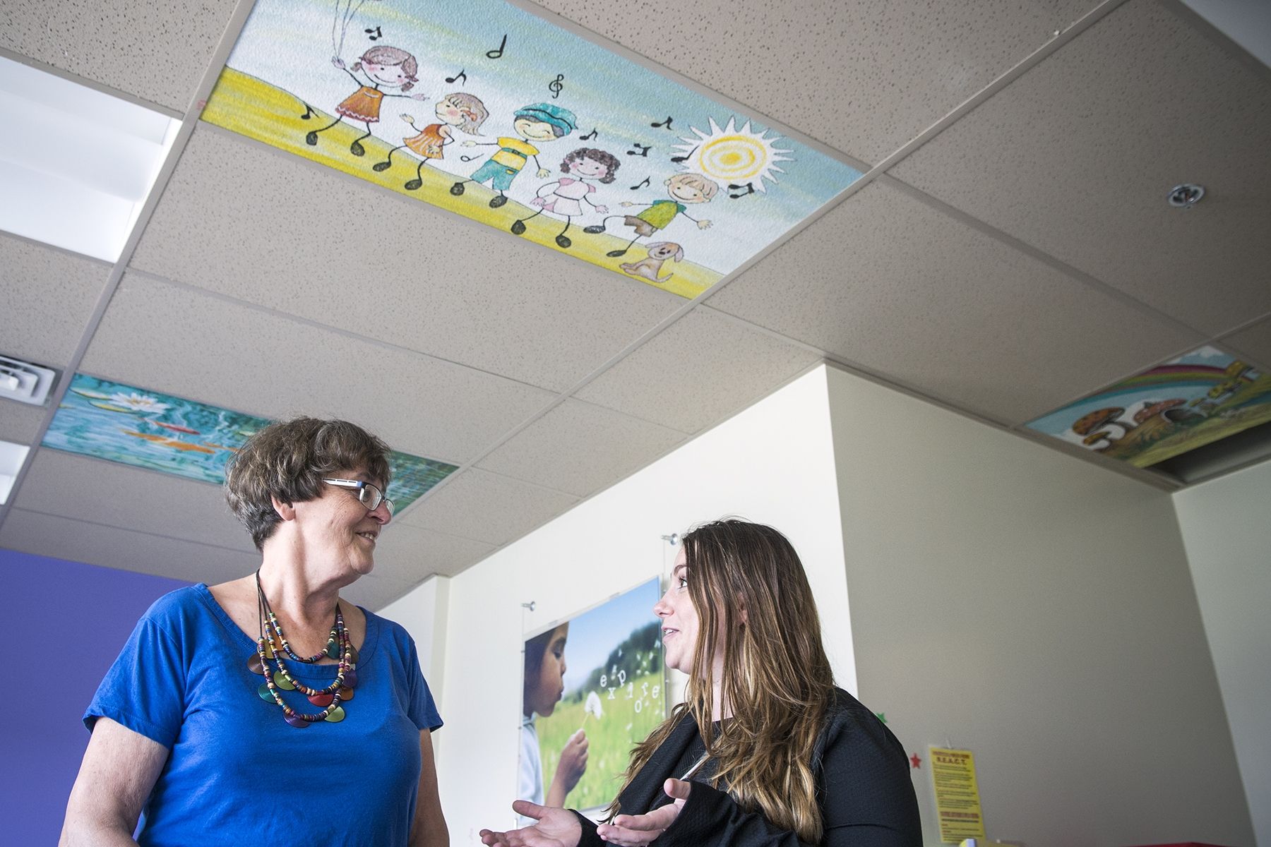 Artist and former patient Donna Scanlan (L) and Pediatrics Program Manager Kerri-Lee Bisonette (R) discuss the new ceiling tiles in the pediatrics unit on Kidd 10. It is one of several areas of the hospital that will benifit from the colourful works of art.