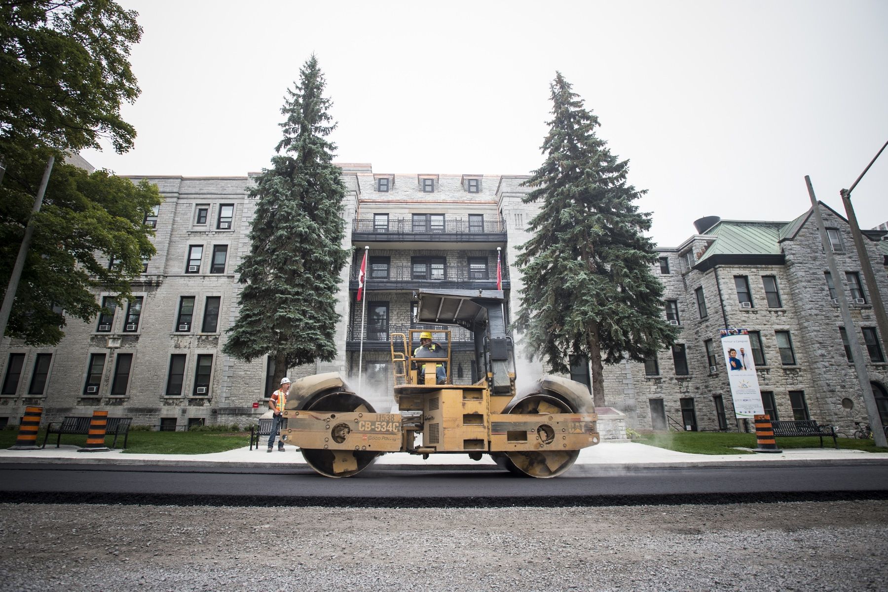 A roller flattens hot, fresh asphalt on Stuart Street in front of the Watkins wing entrance.