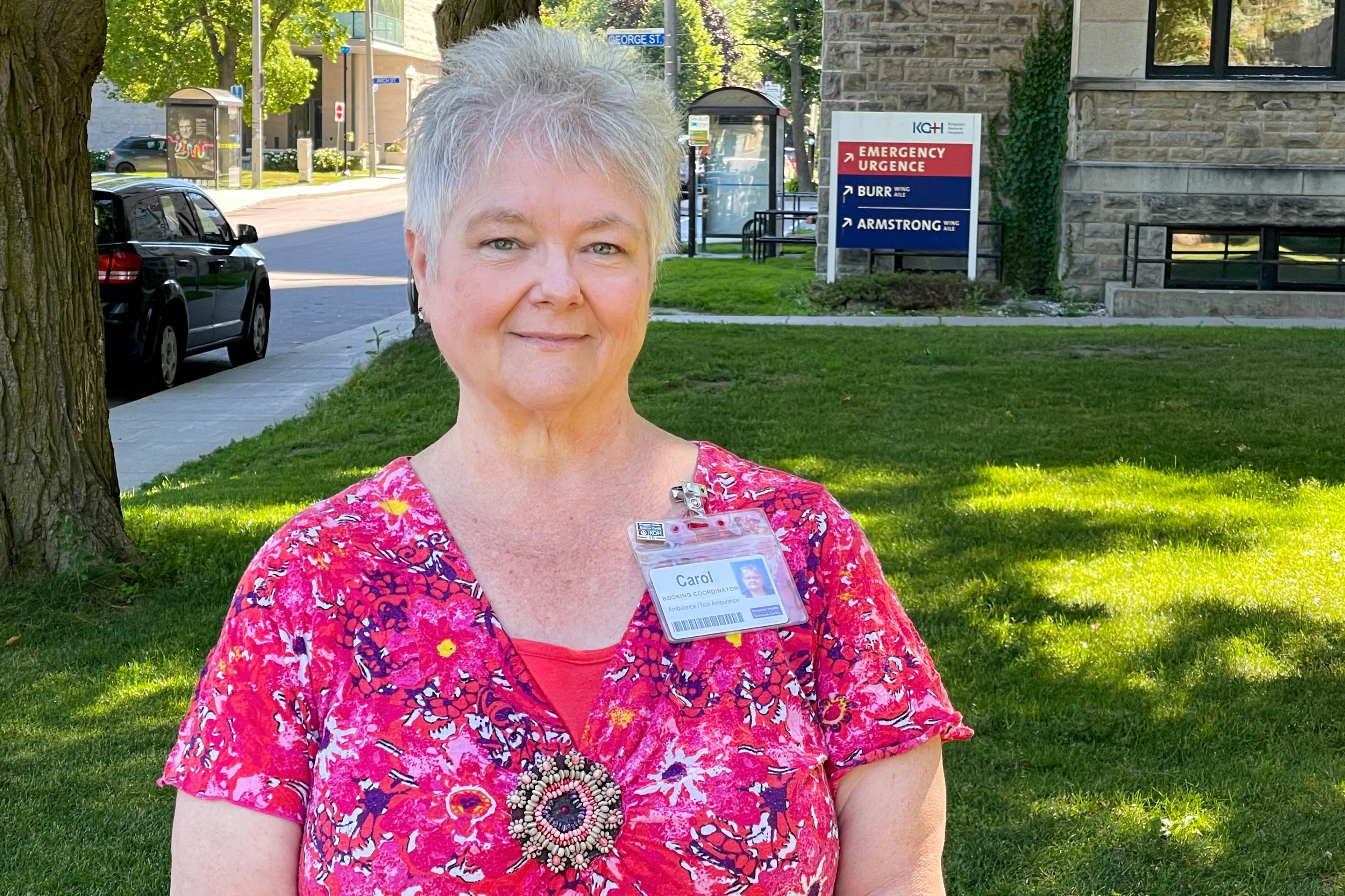 A mid shot image of Carol Foley who has short grey hair and blue eyes, and is wearing a bright pink top.