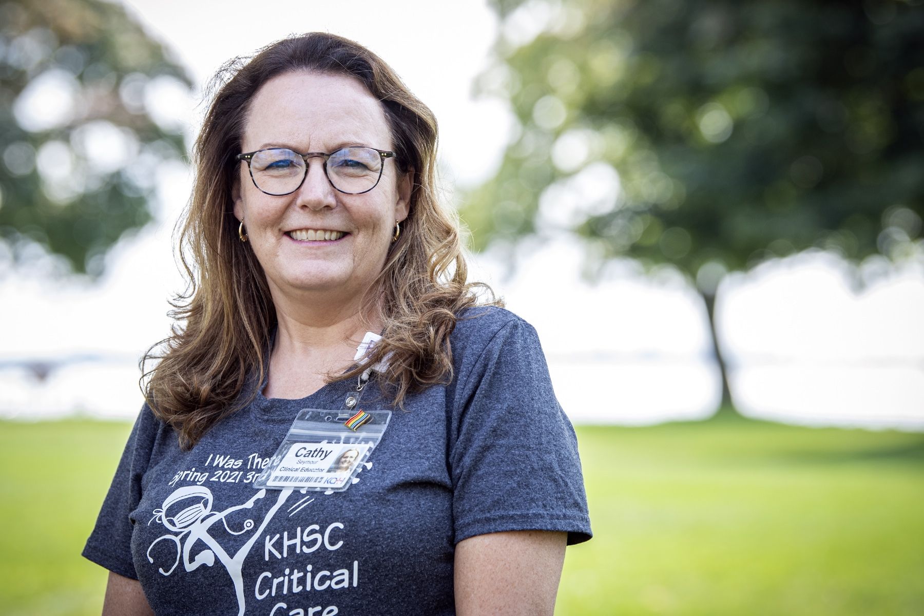 Cathy Seymour has long brown, wavy hair. She has glasses and is wearing a grey t-shirt. She's pictured standing outside the Kingston General Hospital site.