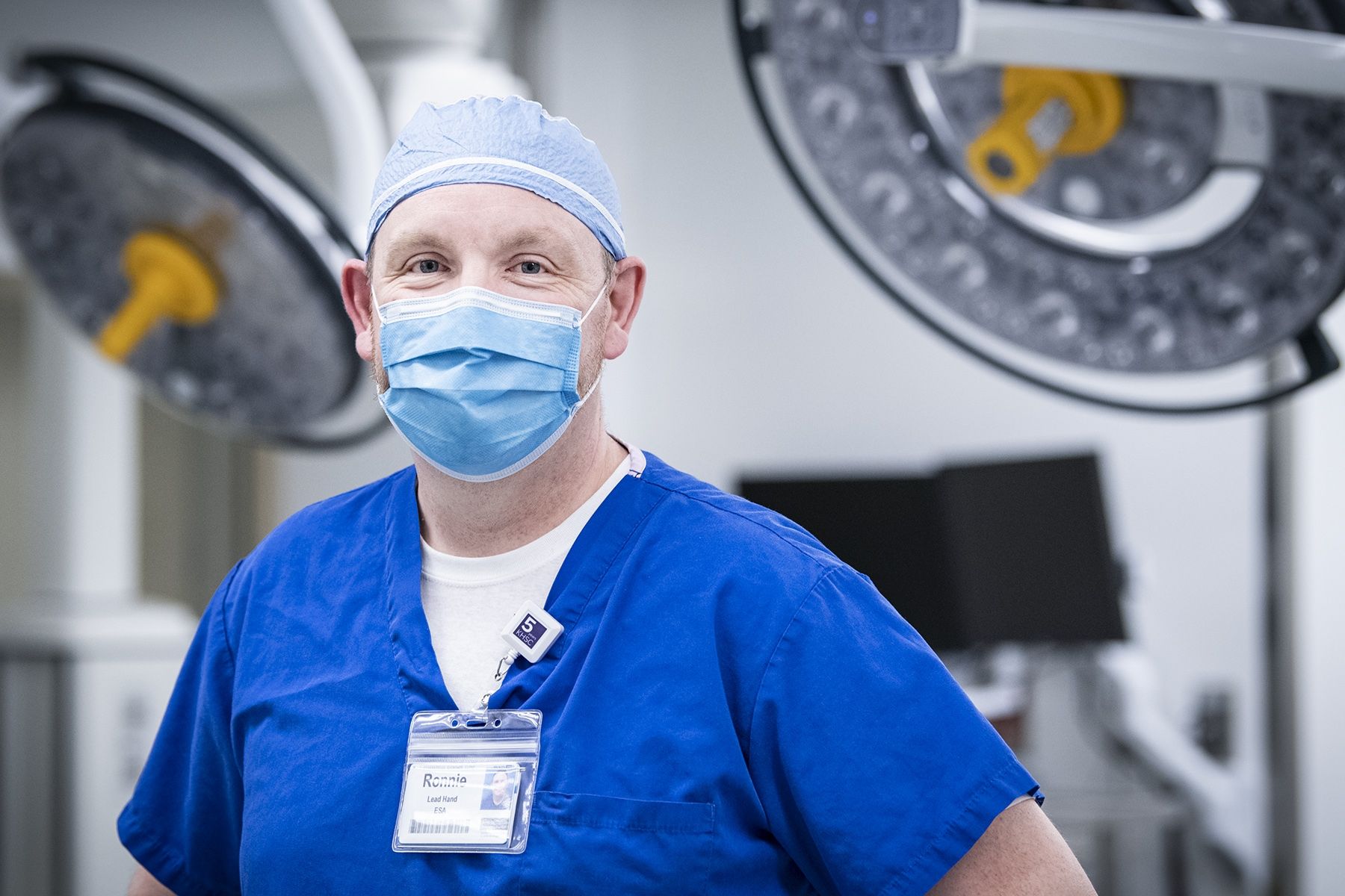 Ronnie Lott is pictured standing inside one of the operating rooms at the KGH site. He has blue eyes and is wearing blue scrubs, a scrub hat and mask. 