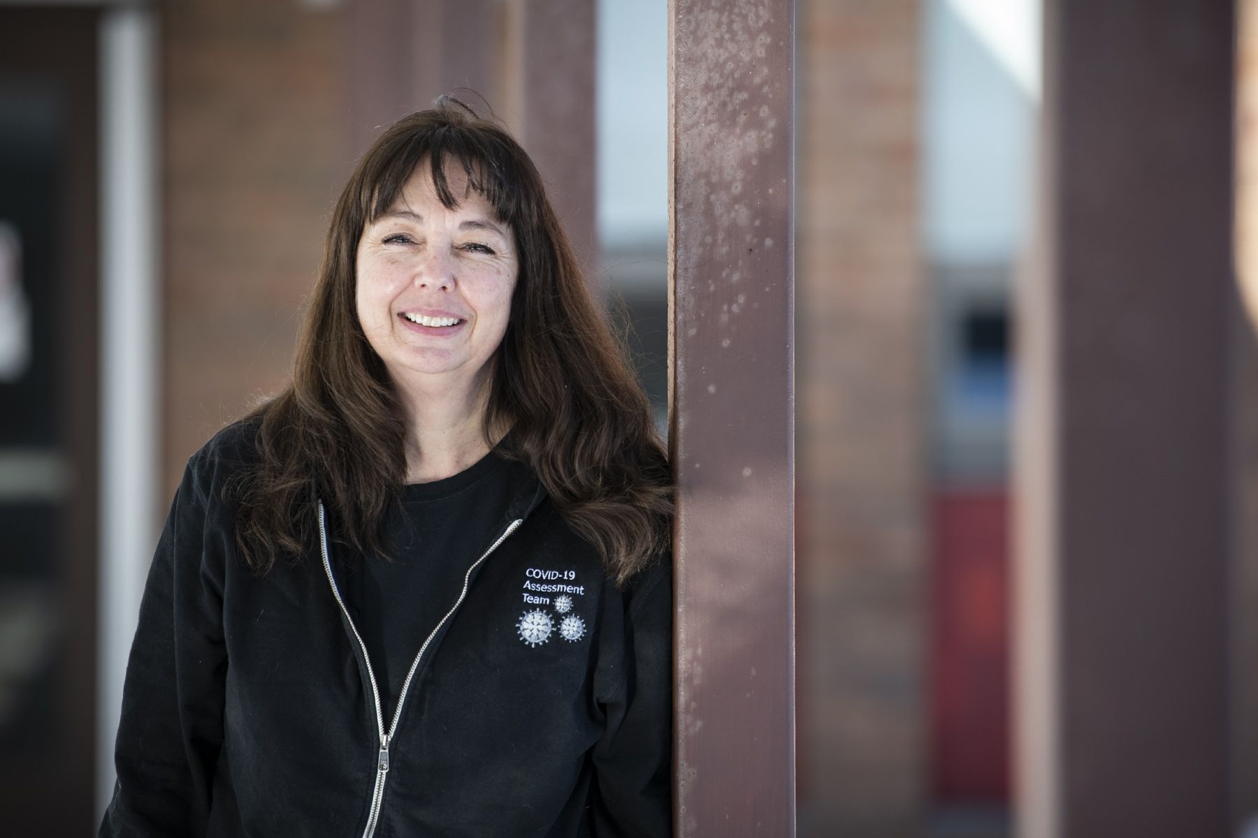 Tricia Anderson is pictured outside the COVID-19 Assessment Centre at the Beechgrove Complex. She has shoulder length, dark brown hair with bangs, and is wearing a black jacket on top of a black shirt.